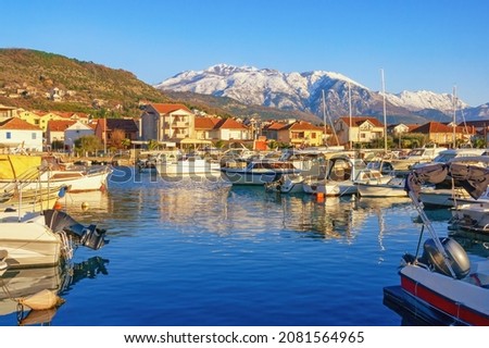 Beautiful Mediterranean landscape on sunny winter day. Fishing boats in harbor and snow-capped mountains. Montenegro, Kotor Bay. Tivat city,  view of marina Kalimanj and mountains of Lovcen