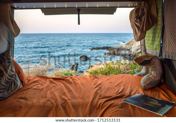 beautiful mediterranean view from a cozy bohemian\
camper van interior. Unmade bed, pillows, van life theme. Vanlife\
lifestyle and travel concept/ young people traveling with camper/\
restored vehicle