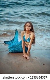 Beautiful mermaid girl on the seashore. Mermaid on the ocean against the background of rocks. Mermaid with a blue tail on the beach. Mermaid on the background of the waves. Siren washed ashore.