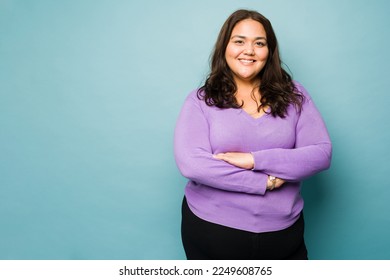Beautiful mexican obese woman with her arms crossed smiling against a studio background with copy space - Shutterstock ID 2249608765