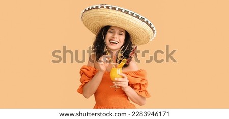 Beautiful Mexican woman in sombrero hat and with cocktail on beige background