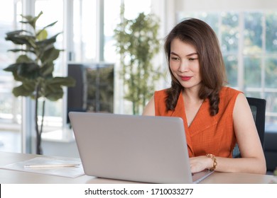 Beautiful Middle Age Asian Businesswoman Sitting At Desk And Using Laptop Notebook Computer In Apartment Or Condominium Living Room With Easy And Happiness. Idea For Work At Home Or Home Base Working.
