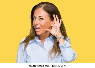 Beautiful middle age business adult woman over isolated background smiling with hand over ear listening an hearing to rumor or gossip. Deafness concept.