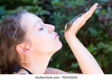 Beautiful Middle Age Caucasian Woman Is Holding A Slug In Her Hand And Forming Her Lips For A Kiss. Picture Taken In Tofino, Vancouver Island, British Columbia, Canada.