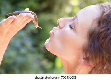 Beautiful Middle Age Caucasian Woman Is Holding A Slug In Her Hand And Forming Her Lips For A Kiss. Picture Taken In Tofino, Vancouver Island, British Columbia, Canada.