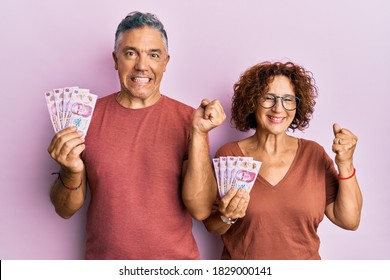 Beautiful Middle Age Couple Holding 50 Mexican Pesos Banknotes Screaming Proud, Celebrating Victory And Success Very Excited With Raised Arm 