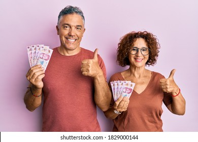 Beautiful Middle Age Couple Holding 50 Mexican Pesos Banknotes Smiling Happy And Positive, Thumb Up Doing Excellent And Approval Sign 