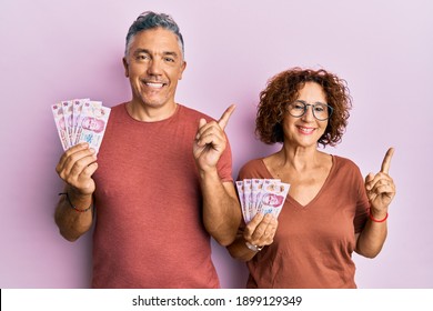 Beautiful Middle Age Couple Holding 50 Mexican Pesos Banknotes Smiling Happy Pointing With Hand And Finger To The Side 