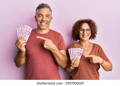 Beautiful Middle Age Couple Holding 50 Mexican Pesos Banknotes Smiling Happy Pointing With Hand And Finger 