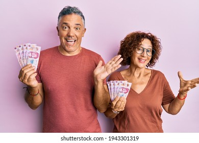 Beautiful Middle Age Couple Holding 50 Mexican Pesos Banknotes Celebrating Achievement With Happy Smile And Winner Expression With Raised Hand 