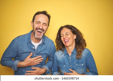 Beautiful middle age couple together standing over isolated yellow background smiling and laughing hard out loud because funny crazy joke with hands on body. - Shutterstock ID 1460198714