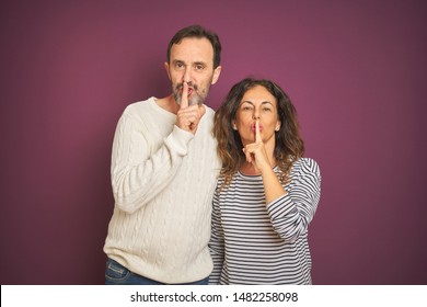 Beautiful middle age couple wearing winter sweater over isolated purple background asking to be quiet with finger on lips. Silence and secret concept. - Shutterstock ID 1482258098