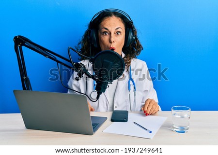Beautiful middle age doctor woman working at radio studio scared and amazed with open mouth for surprise, disbelief face 