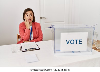 Beautiful Middle Age Hispanic Woman At Political Election Sitting By Ballot Looking Stressed And Nervous With Hands On Mouth Biting Nails. Anxiety Problem. 