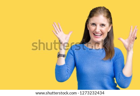Beautiful middle age mature woman wearing winter sweater over isolated background celebrating mad and crazy for success with arms raised and closed eyes screaming excited. Winner concept