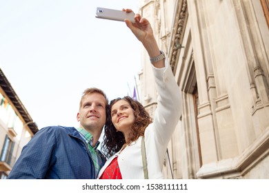 Beautiful Middle Age Tourist Couple On  Winter City Break Holiday Sightseeing Together, Using Technology Smartphone Smiling, Taking Selfies Outdoors. Fun Travel Vacation, Leisure Recreation Lifestyle.