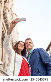 Beautiful Middle Age Tourist Couple On Winter City Break Holiday Sightseeing Together, Using Technology Smartphone Smiling, Taking Selfies Outdoors. Fun Travel Vacation, Leisure Recreation Lifestyle.