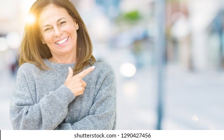 Beautiful middle age woman wearing winter sweater over isolated background cheerful with a smile of face pointing with hand and finger up to the side with happy and natural expression on face