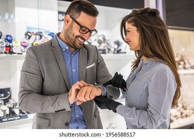 Beautiful Middle Age Woman Working In Jewelry Store. She Is Holding And Showing Expensive Watch To Male Buyer.