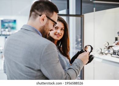 Beautiful Middle Age Woman Working In Jewelry Store. She Is Holding And Showing Expensive Watch To Male Buyer.