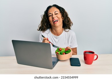 Beautiful Middle Age Woman Working At The Office Eating Healthy Salad Smiling And Laughing Hard Out Loud Because Funny Crazy Joke. 