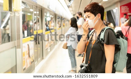 Beautiful middle aged Asian female traveller cover mouth and cough, wear medical face mask to protect from infection of viruses, pandemic, Covid-19 outbreak and epidemic, Stop asian hate, Anti-asian.