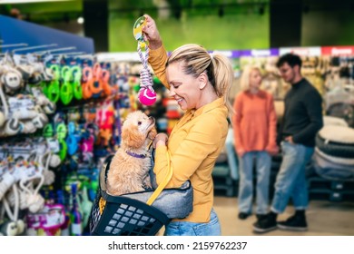 Beautiful middle aged blond woman buying accessories and food for her poodle puppy in pet shop.