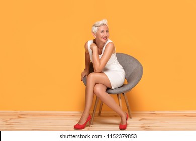 Beautiful middle aged blonde lady smiling, relaxing. Woman wearing red fashionable high heels posing on yellow studio background.
