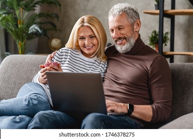 Beautiful Middle Aged Couple Using Laptop And Smiling While Resting On Couch At Home