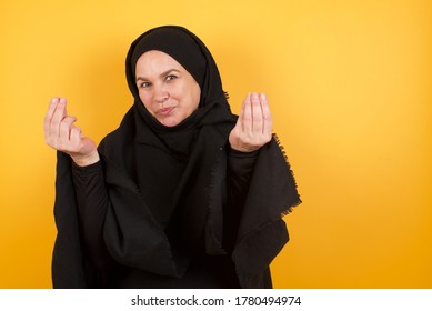 Beautiful Middle Aged Muslim Woman Wearing Black Hijab Over Yellow Background Doing Money Gesture With Hands, Asking For Salary Payment, Millionaire Business