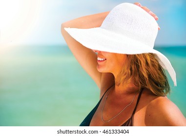 Beautiful Middle Aged Woman In A Big White Hat Tanning On The Beach. Beauty Female Portrait Over Blue Ocean Background. Summer Holidays, Vacation Concept. Relaxing On Resort Under The Hot Sun. Suntan