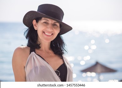 Beautiful Middle Aged Woman With Black Hat Standing In Swimwear On The Wooden Dock, Smiling. Summer Vacation Concept