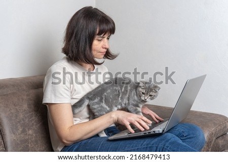 Beautiful middle aged woman with a cutecat works at home on a laptop. Middle-aged woman works remotely. Workplace concept at home with pets. Pets are part of the family
