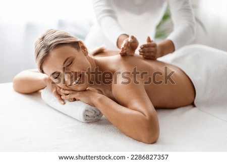 Beautiful Middle Aged Woman Enjoying Professional Wellness Massage In Spa Salon, Closeup Shot Of Therapist Lady Massaging Back Of Attractive Mature Female Lying On Table With Closed Eyes