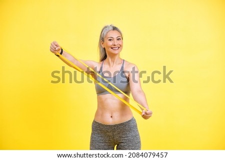 Beautiful middle aged woman making sport at the gym. Senior female model posing for a body positive and self acceptance concept photoshooting on colored backgrounds