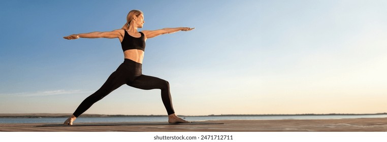 Beautiful Middle Aged Woman Practicing Yoga Outdoors, Standing In Warrior Pose On Fitness Mat, Sporty Female In Activewear Training On Wooden Pier Near Sea, Enjoying Healthy Lifestyle, Copy Space - Powered by Shutterstock