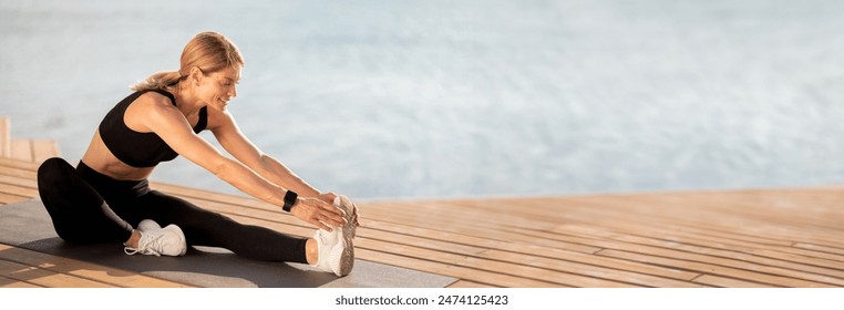 Beautiful Middle Aged Woman Stretching Legs While Training Outdoors On The Pier, Smiling Sporty Female Sitting On Yoga Mat Near Water And Doing Fitness Exercises, Touching Toes With Hands, Copy Space - Powered by Shutterstock