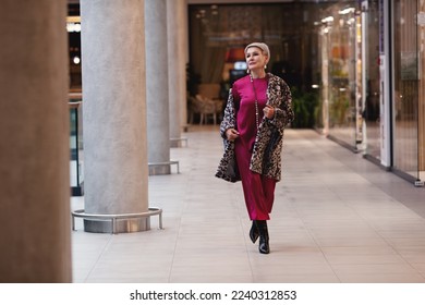 Beautiful middle aged Woman Wearing Fashionable Clothes long burgundy silk dress, leopard print coat jacket, black boots. Female stylish Model walking mall shopping center. Fashion outfit - Shutterstock ID 2240312853