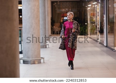 Beautiful middle aged Woman Wearing Fashionable Clothes long burgundy silk dress, leopard print coat jacket, black boots. Female stylish Model walking mall shopping center. Fashion outfit