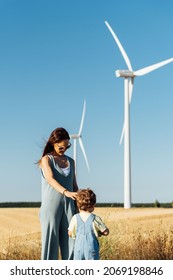 Beautiful Middle Aged Young Mother Woman In Wind Farm With Windmills In Background With Her Three Year Old Son. Renewable Energy Concept