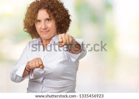 Beautiful middle ager senior businees woman over isolated background Punching fist to fight, aggressive and angry attack, threat and violence