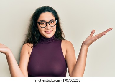 Schöne mittelöstliche Frau mit lockeren Kleidung und Brillen ahnungslos und verwirrt mit offenen Armen, keine Idee und zweifelhaftes Gesicht. 