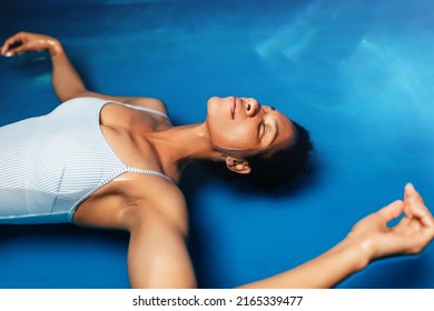 Beautiful middle-aged African American woman floating in tank filled with dense salt water used in meditation, therapy and alternative medicine. 