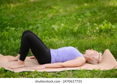 Beautiful middle-aged European woman practicing yoga in park. Dead Body Pose or Savasana Pose. Woman lies on yoga mat, meditates, relaxes and feels comfortable. Concept of health, yoga in nature - Powered by Shutterstock