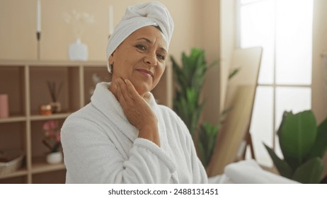 A beautiful middle-aged hispanic woman in a wellness spa room wearing a white robe and towel on her head, radiating confidence and relaxation. - Powered by Shutterstock