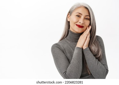 Beautiful Middle-aged Japanese Woman, Wearing Red Lipstick Makeup, Smiling Happy, Holding Hands Near Healthy Fresh Face, Standing Over White Background.