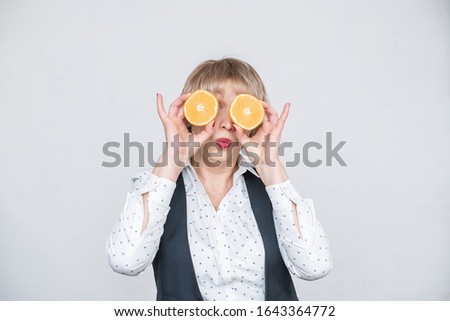 A beautiful middle-aged woman comically and emotionally puts orange slices with her hands to her eyes on a white background in the Studio.