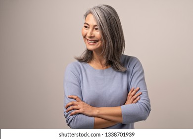 Beautiful Middle-Aged Woman With Crossed Arms Looks Aside. Charming Elderly Asian Woman With Crossed Arms Smiles While Looking Sideways.