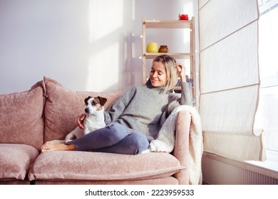 Beautiful middle-aged woman with dog at home sitting on couch in front of window, relaxing in her living room  - Powered by Shutterstock