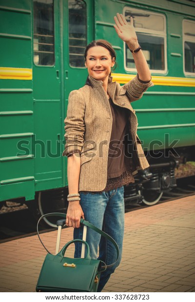beautiful middle-aged woman goes on a\
trip by railway and waving good-bye on the background of green\
passenger car of the train. instagram image filter retro\
style